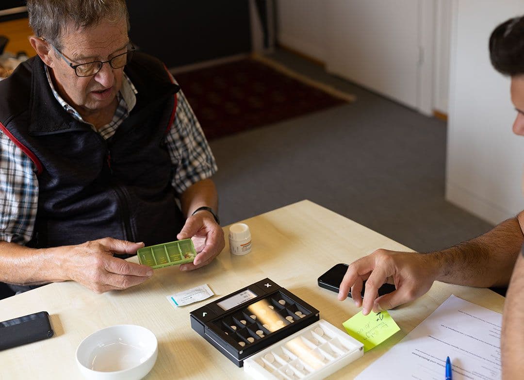 Teilnehmer und Begleitperson betrachten Pillbox-Prototypen während eines Adherlo Usability-Tests im Alltag